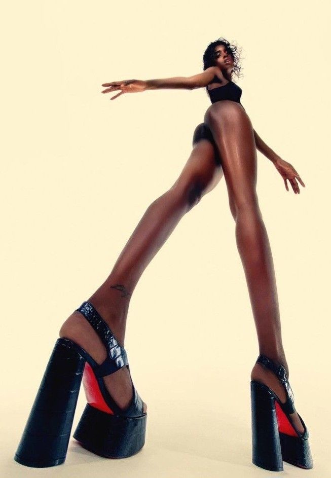 Low-angle fashion portrait of a woman in towering black platform heels against a cream background